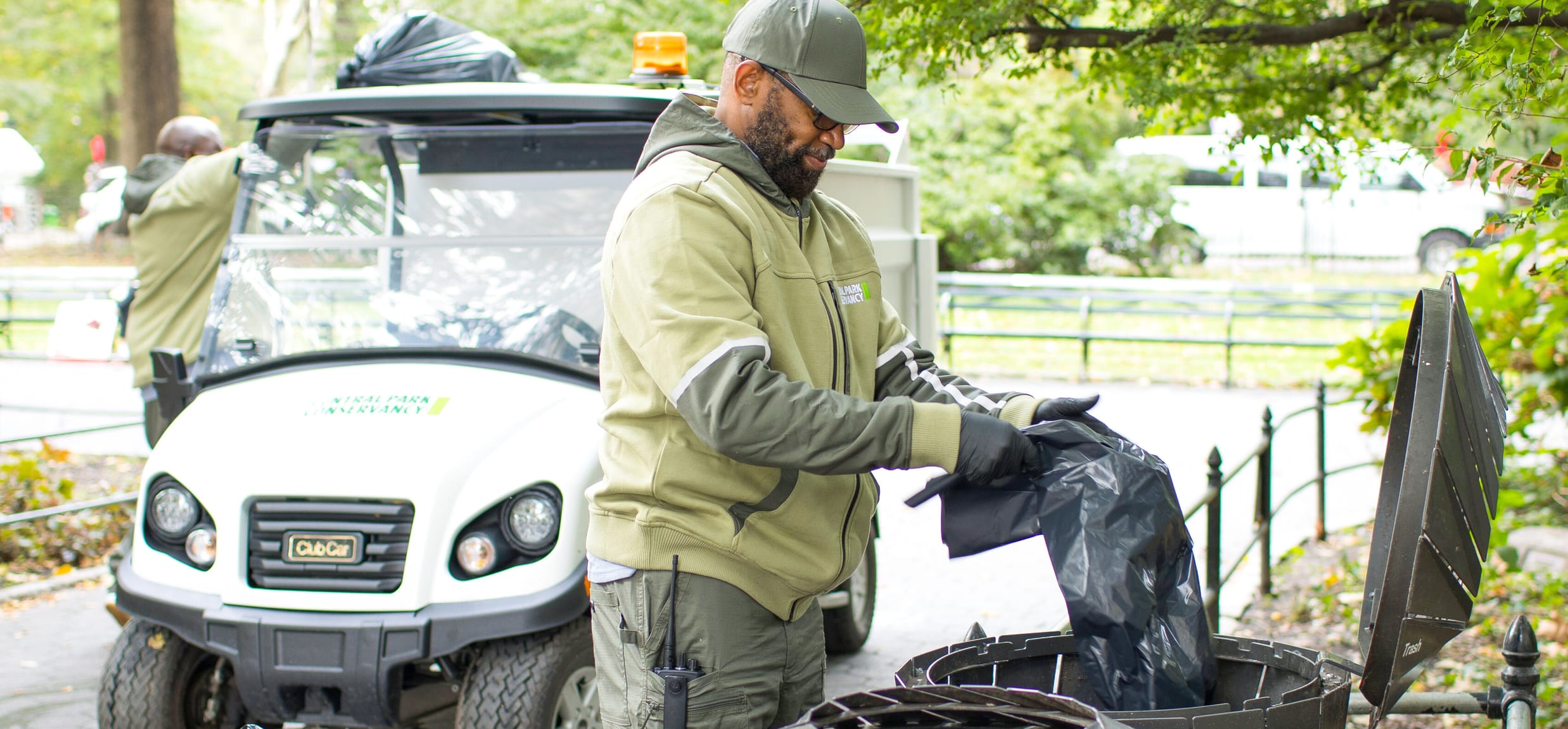 A Conservancy staff member, dressed in the organization's green uniform and hat, puts a new garbage bag in one of Central Park's receptacles.